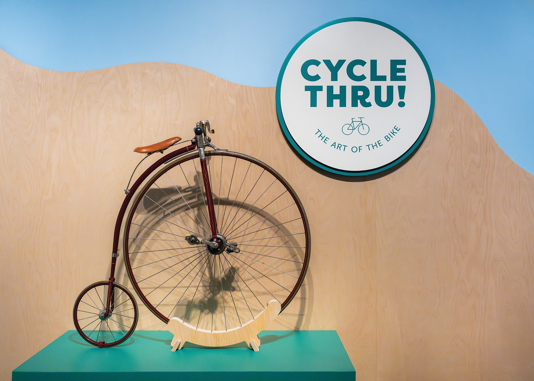 Penny-farthing bicycle in a museum exhibit with a round sign reading 