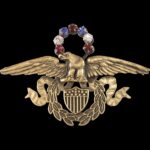 Costume jewelry pin with a gold tone eagle with spread wings, shield, and wreath topped with an arc of red, white, and blue stones