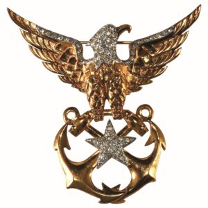 Costume jewelry pin in the form of a gold tone eagle with spread wings grasping 2 crossed anchors with a star, sparkly stone accents