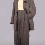 Charcoal gray pinstriped zoot suit consisting of a brimmed hat, open a jacket, and trosers on a mannequin