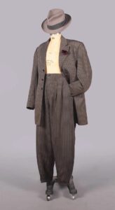 Charcoal gray pinstriped zoot suit consisting of a brimmed hat, open a jacket, and trosers on a mannequin