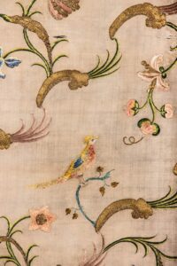 Section of cream cloth embroidered with colorful birds perching on flowering branches