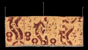 Golden yellow fabric piece with allover red pattern held up by 3 strings