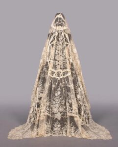 Long ivory lace veil on a mannequin, with corners trailing on the floor