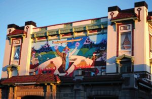 Colorful mural between 2 windows on the second story of a building facade