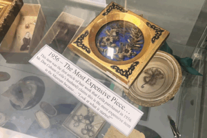 Wreath in a square gold frame in a glass museum case with a label in front