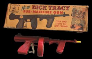 Red toy water gun under a rectangular box labeled "New Dick Tracy Sub-Machine Gun"