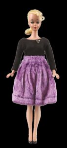 Doll with blonde ponytail wearing a black top and purple skirt